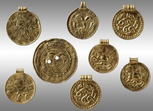 8 goldene Münzen, alle sind mit unterschiedlichen Mustern verziert, eine Münze ist größer als die anderen und hat 2 kleine Löcher, die anderen Münzen haben alle eine Öse am oberen Rand.