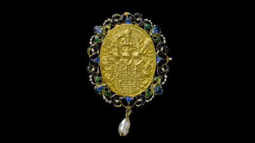 Rückseite einer goldenen, ovalförmigen Münze, bedruckt mit einem Wappen, mit filigraner Randverzierung in blau und grün und einer an der Unterseite befestigten Perle.